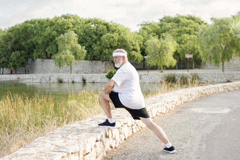 Senior man stretches deeply by a river to improve mobility